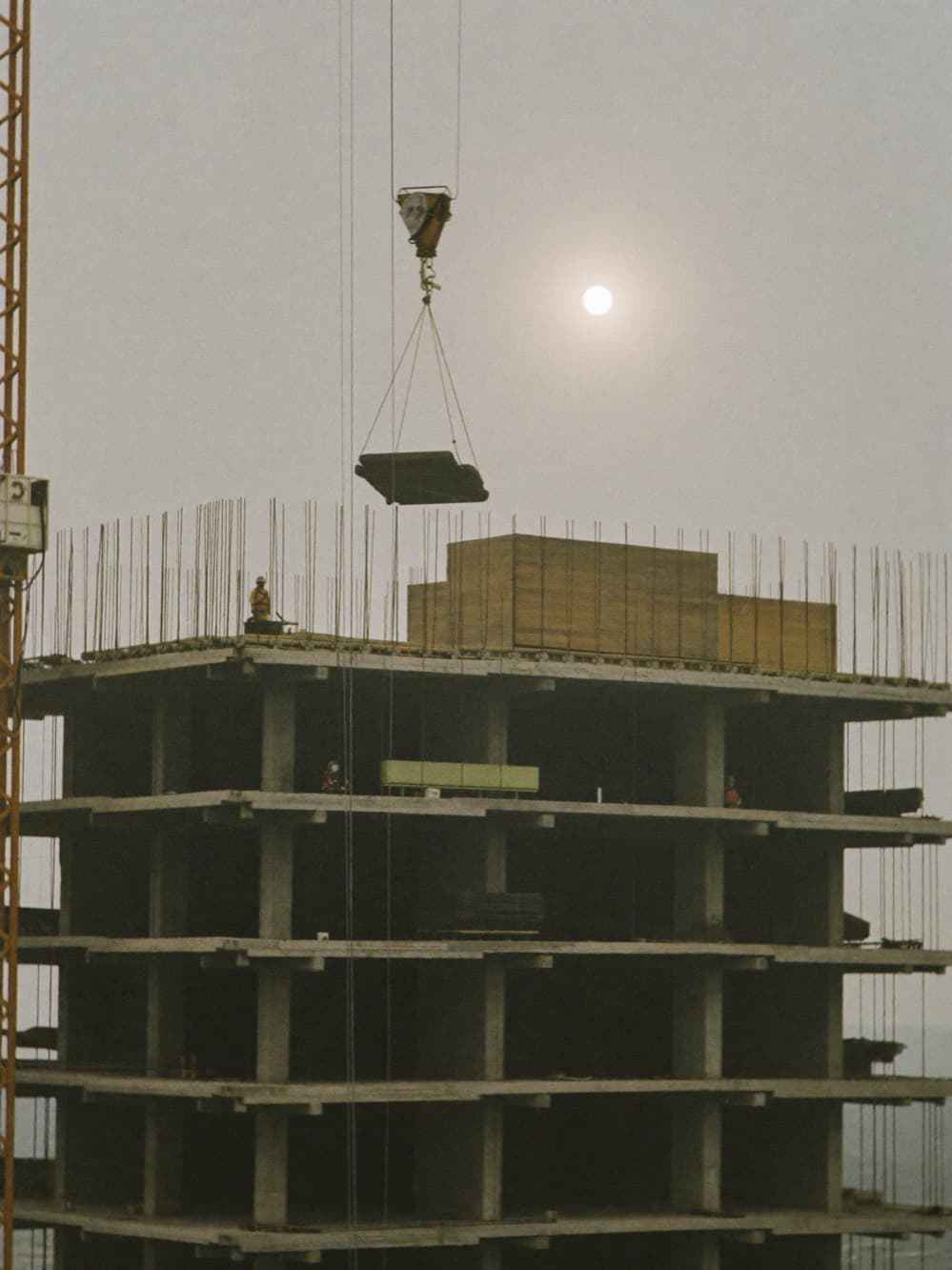 Tower crane lifting materials above the concrete frame of a commercial high-rise under construction