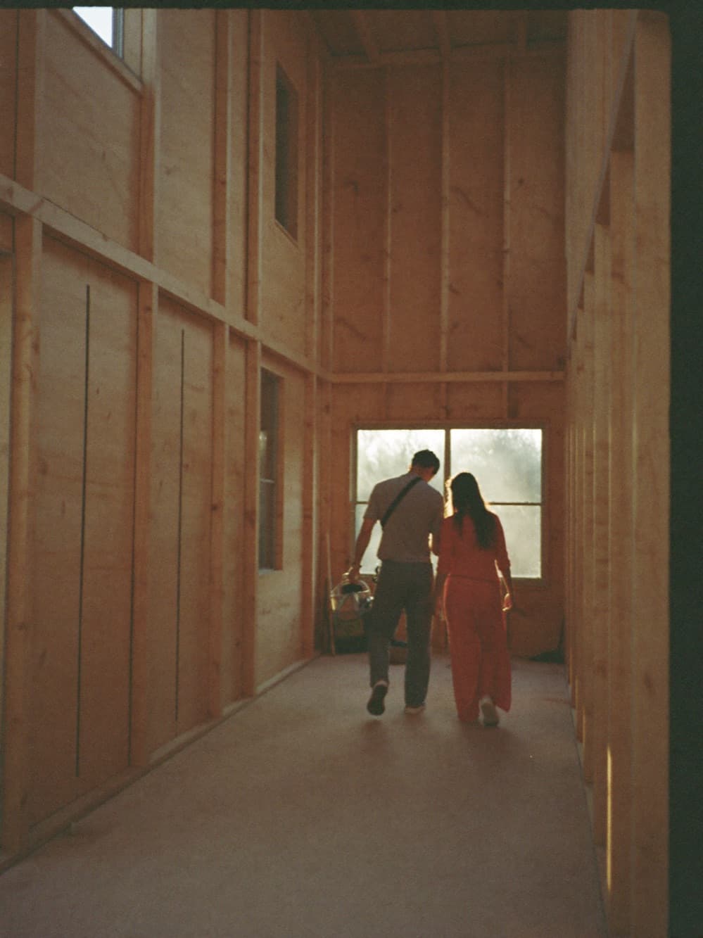 Custom home builder walking clients through the timber-framed great room of their home under construction at golden hour