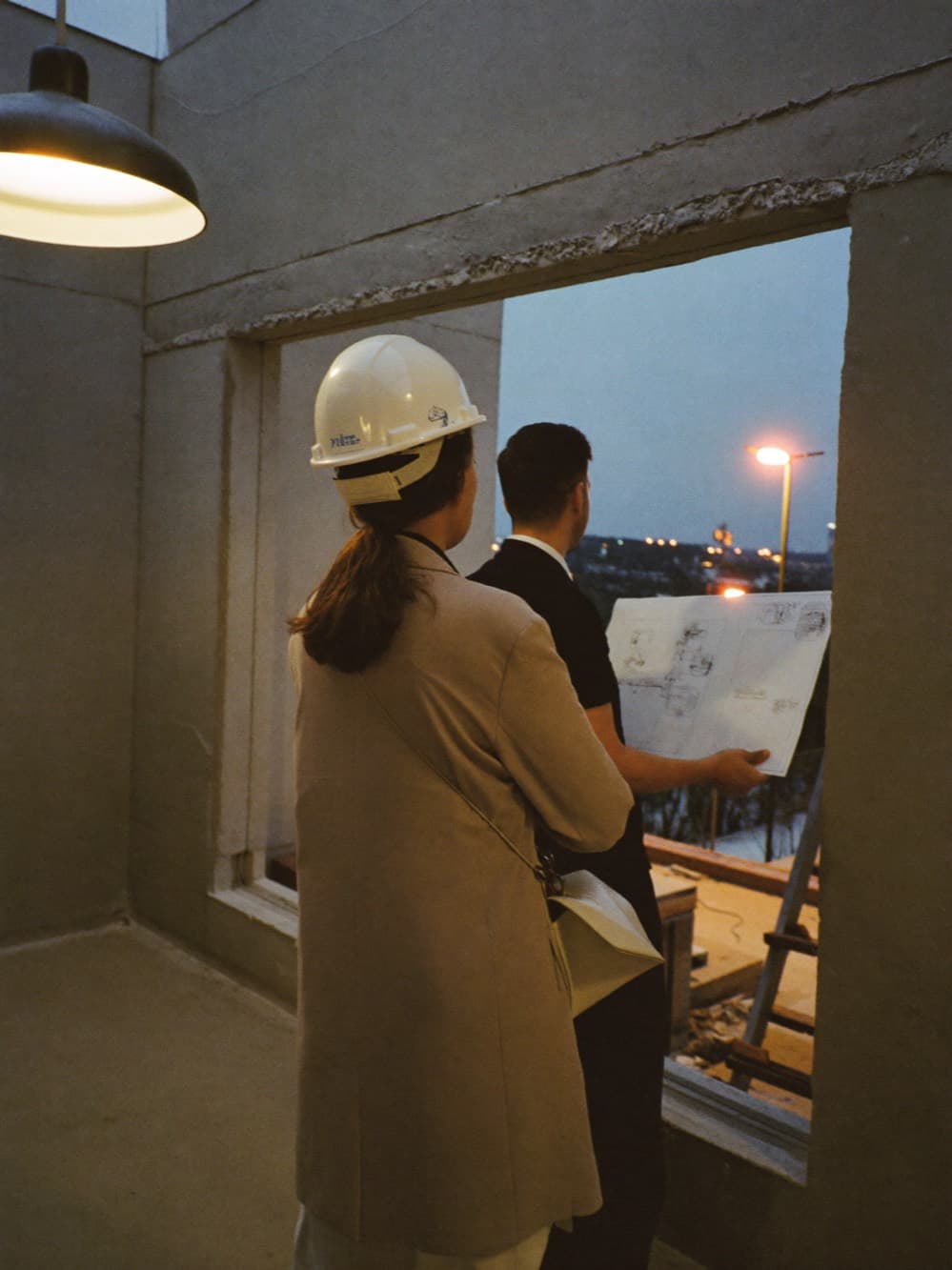 Property owner and site engineer reviewing plans inside a building shell at dusk overlooking the city