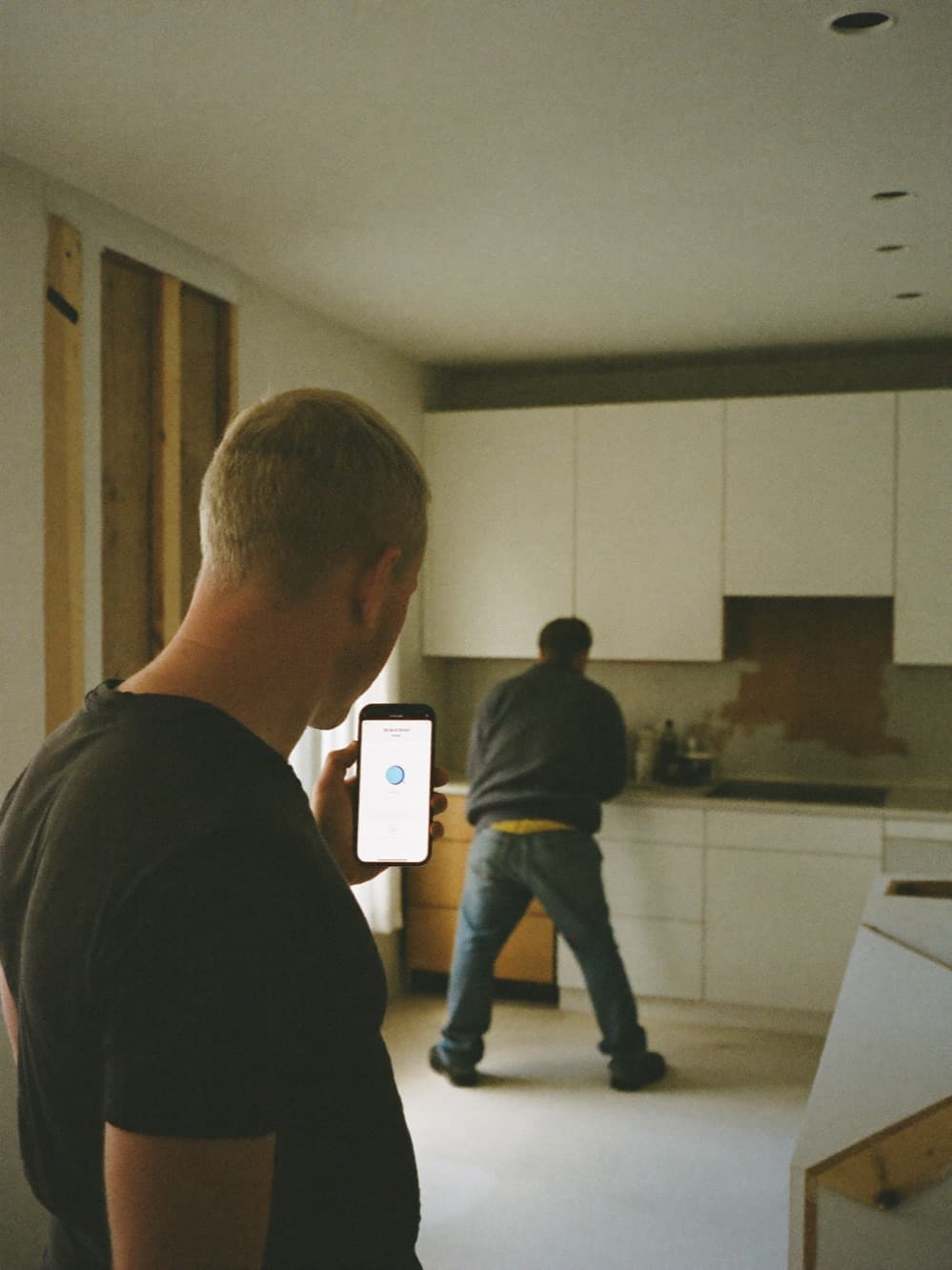 Remodeling contractor showing a homeowner a progress update on a phone in a kitchen mid-renovation