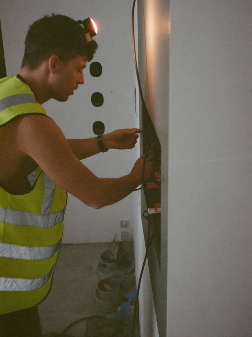 Electrician with a headlamp wiring an electrical panel in an unfinished commercial interior