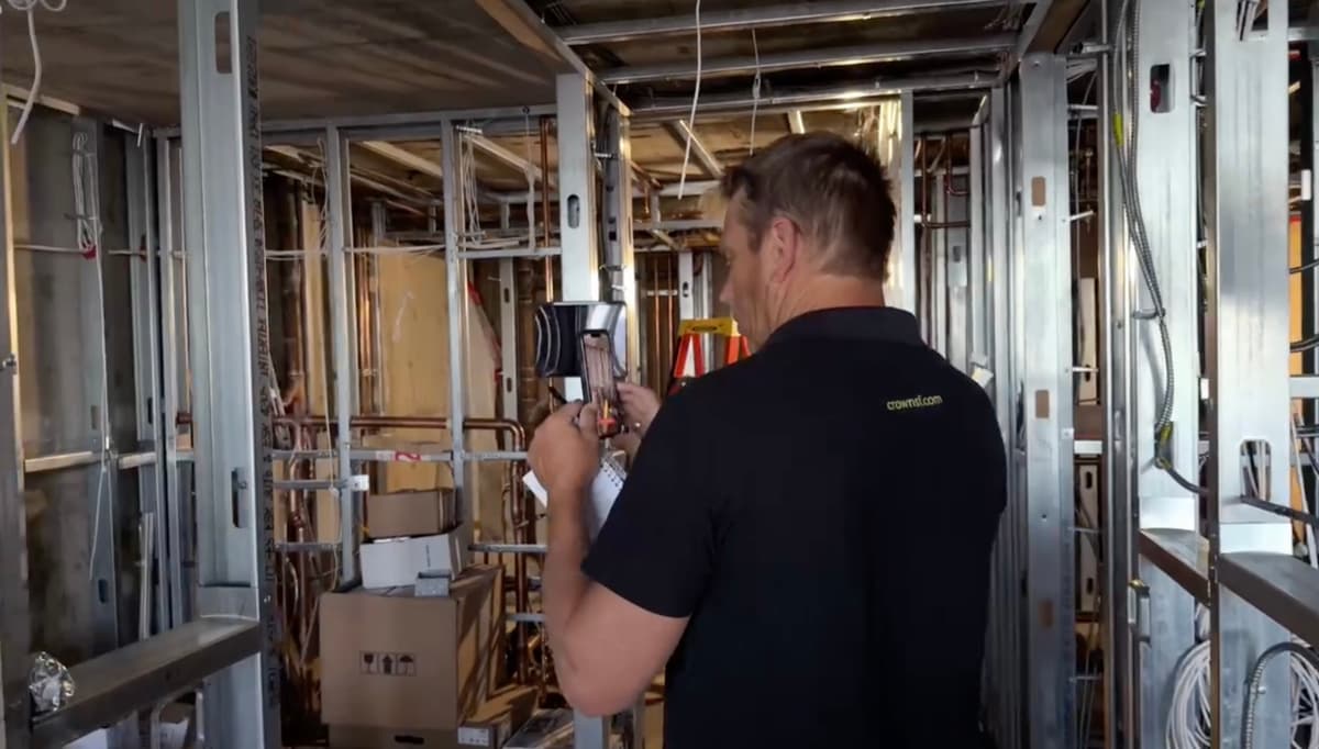 Crown Construction superintendent filming a phone walkthrough on a stud-framed jobsite